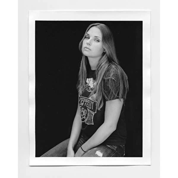 Monochrome portrait of a seated young woman wearing a Led Zeppelin t-shirt and distressed jeans against a solid black backdrop.
