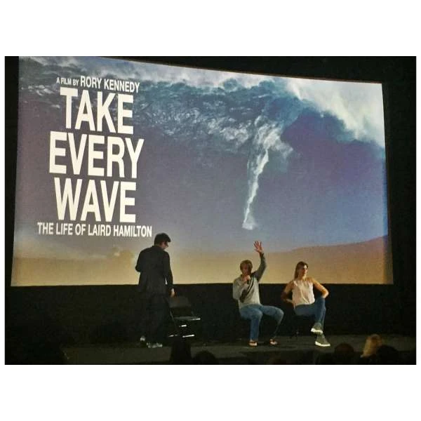 Group of adults seated on a stage in front of a screen showing 'Take Every Wave: The Life of Laird Hamilton' movie poster.