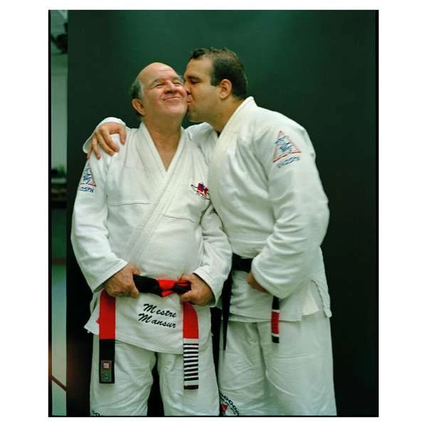 Two adult males in judo uniforms embrace indoors, one kissing the other's cheek, symbolizing camaraderie and respect in martial arts.