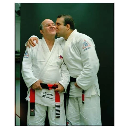 Two adult males in judo uniforms embrace indoors, one kissing the other's cheek, symbolizing camaraderie and respect in martial arts.