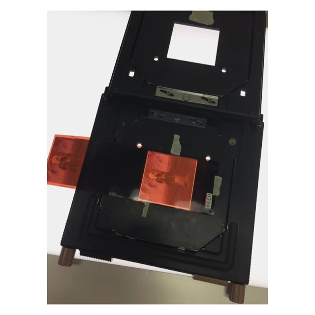 Film negative carrier holding film negatives against a white background. Film negatives are orange with visible silhouette of a person.
