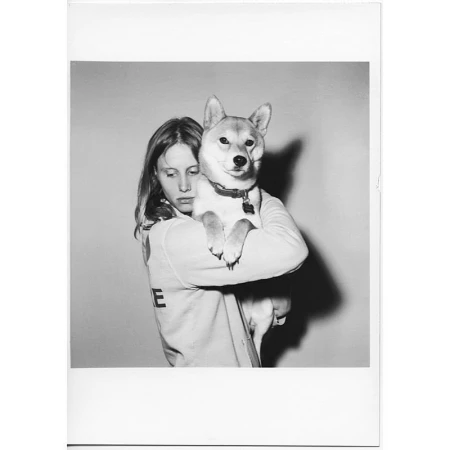 Black and white portrait of a woman holding a Shiba Inu dog, both facing forward in an indoor studio setting with neutral backdrop.