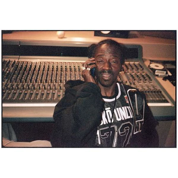 Elderly African-American man in a music studio using a smartphone. Wearing a jersey, he's in front of a mixing console.