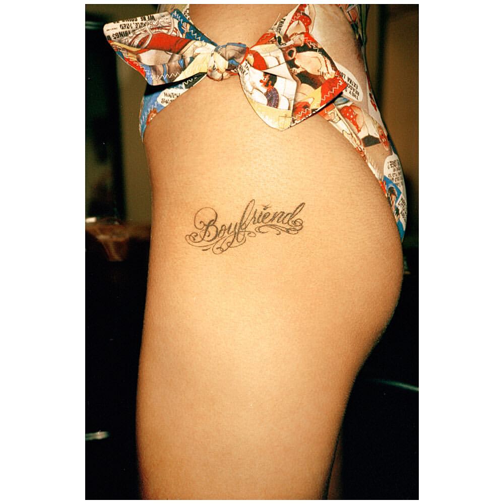 Torso of a woman with a tattoo of the word "Boyfriend" on her hip, wearing a bow-tied swimsuit bottom with a comic book pattern.