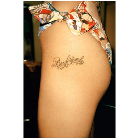 Torso of a woman with a tattoo of the word "Boyfriend" on her hip, wearing a bow-tied swimsuit bottom with a comic book pattern.