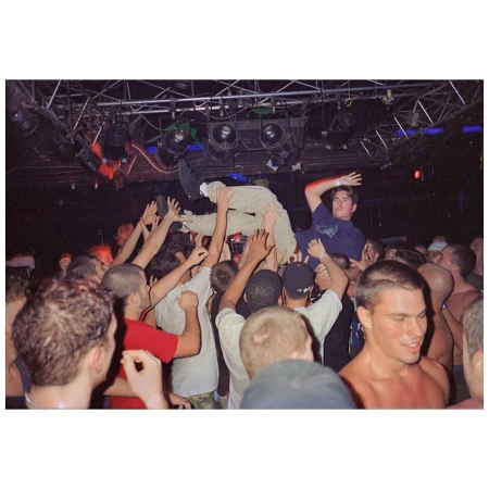Crowd surfing at a music event, with several people holding up a man as another man stands above them at an indoor venue.