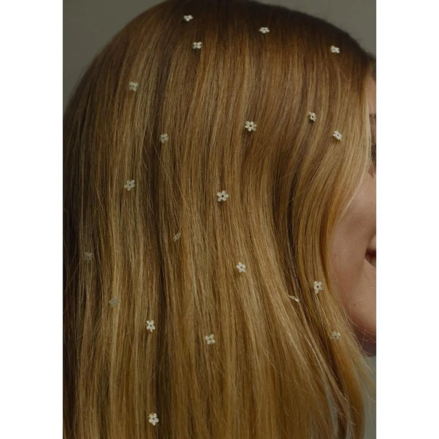 Close-up on a woman's long blonde hair adorned with small white floral hair accessories, set against a neutral background.