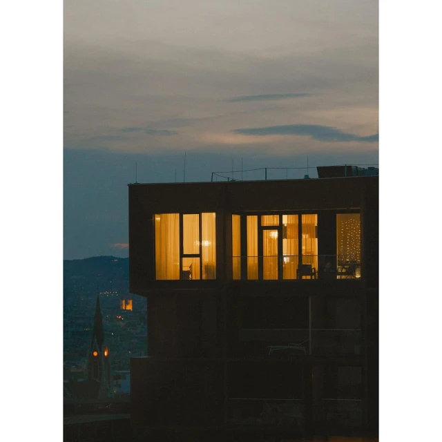 Exterior view of a modern building with illuminated windows during twilight, showcasing architectural design and urban living against a dusky sky.