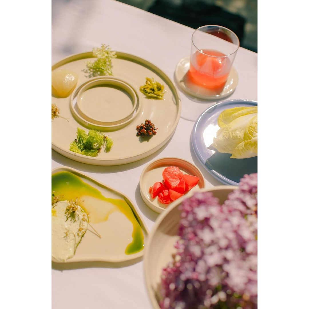 Overhead shot of an arrangement of plates with various foods, including vegetables and a pink drink, set on a white table.
