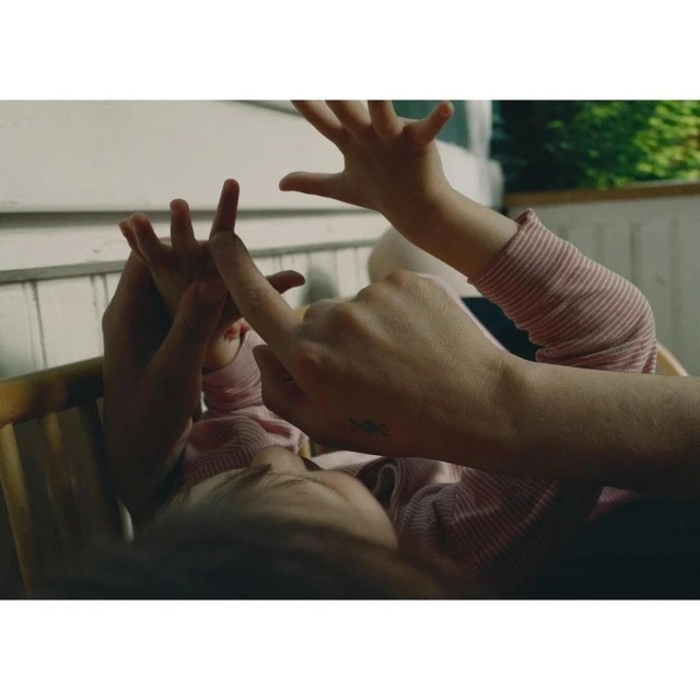 Close-up of a toddler lying down while an adult holds the child's hands. The background is a porch with a white railing.