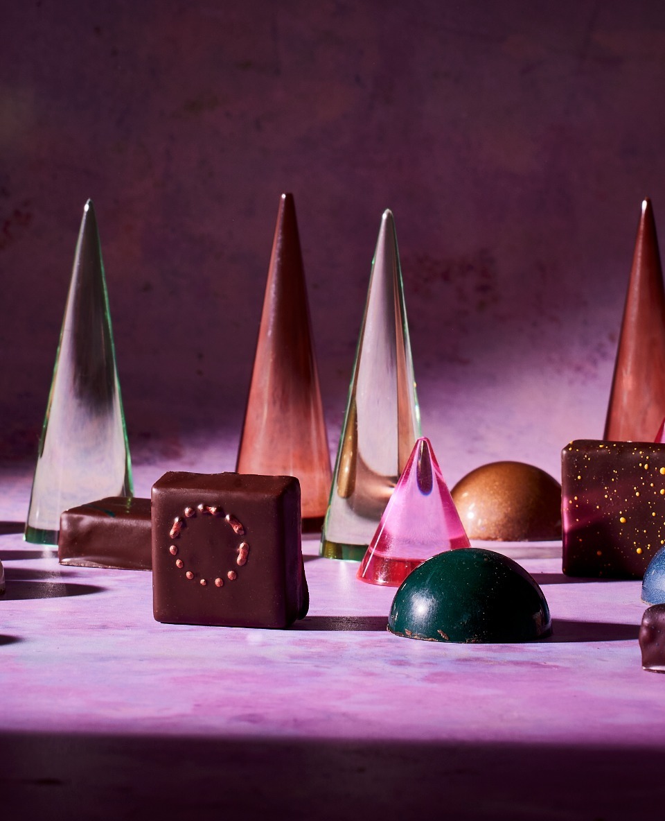 Geometric chocolates: an assortment of artisan chocolate bonbons in geometric shapes on a purple surface with studio lighting. Food photography.