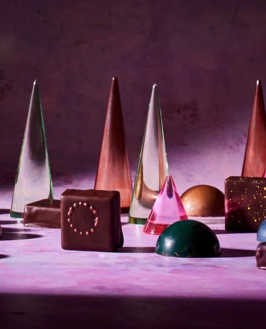 Geometric chocolates: an assortment of artisan chocolate bonbons in geometric shapes on a purple surface with studio lighting. Food photography.