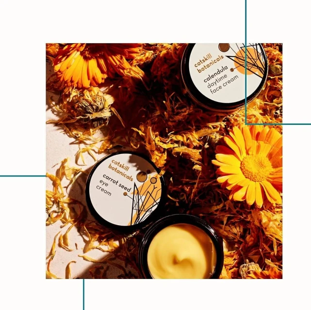 Several jars of botanical skincare products are showcased with calendula flowers and petals creating a natural, vibrant beauty product display.