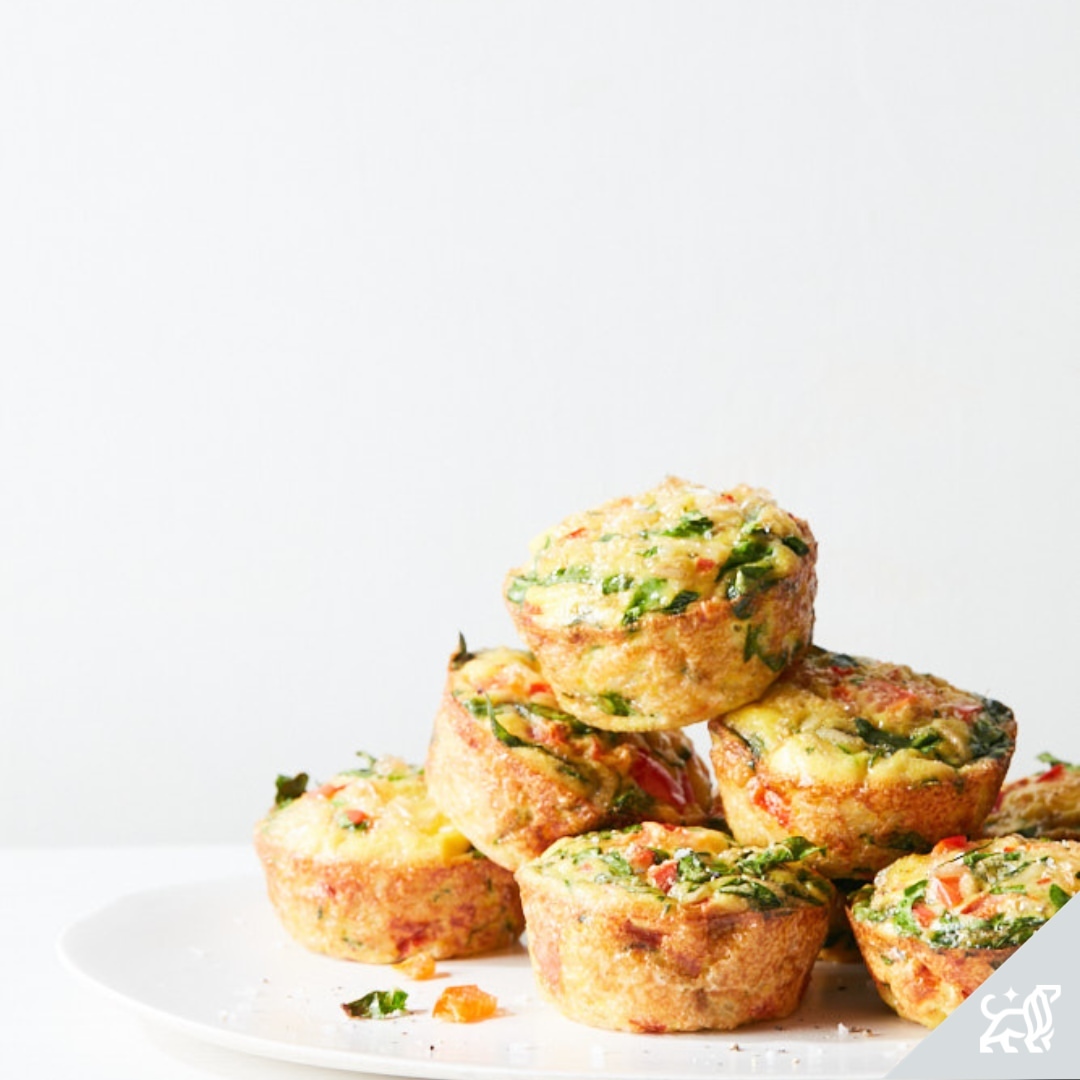 Pile of savory egg muffins with visible spinach and red pepper, arranged on a white plate against a bright, neutral background.