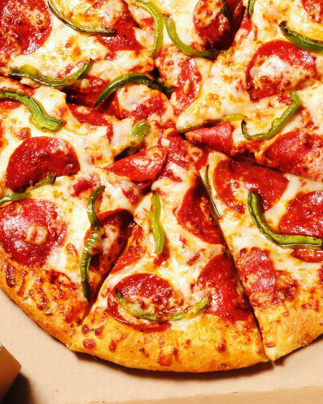 Overhead close-up of a pepperoni pizza with green bell peppers cut into slices showing melted cheese, sauce, and crust.