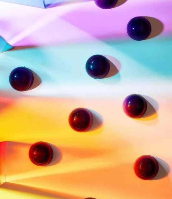 Abstract studio shot with translucent geometric shapes casting rainbow-colored shadows on a white surface, featuring dark purple spheres.
