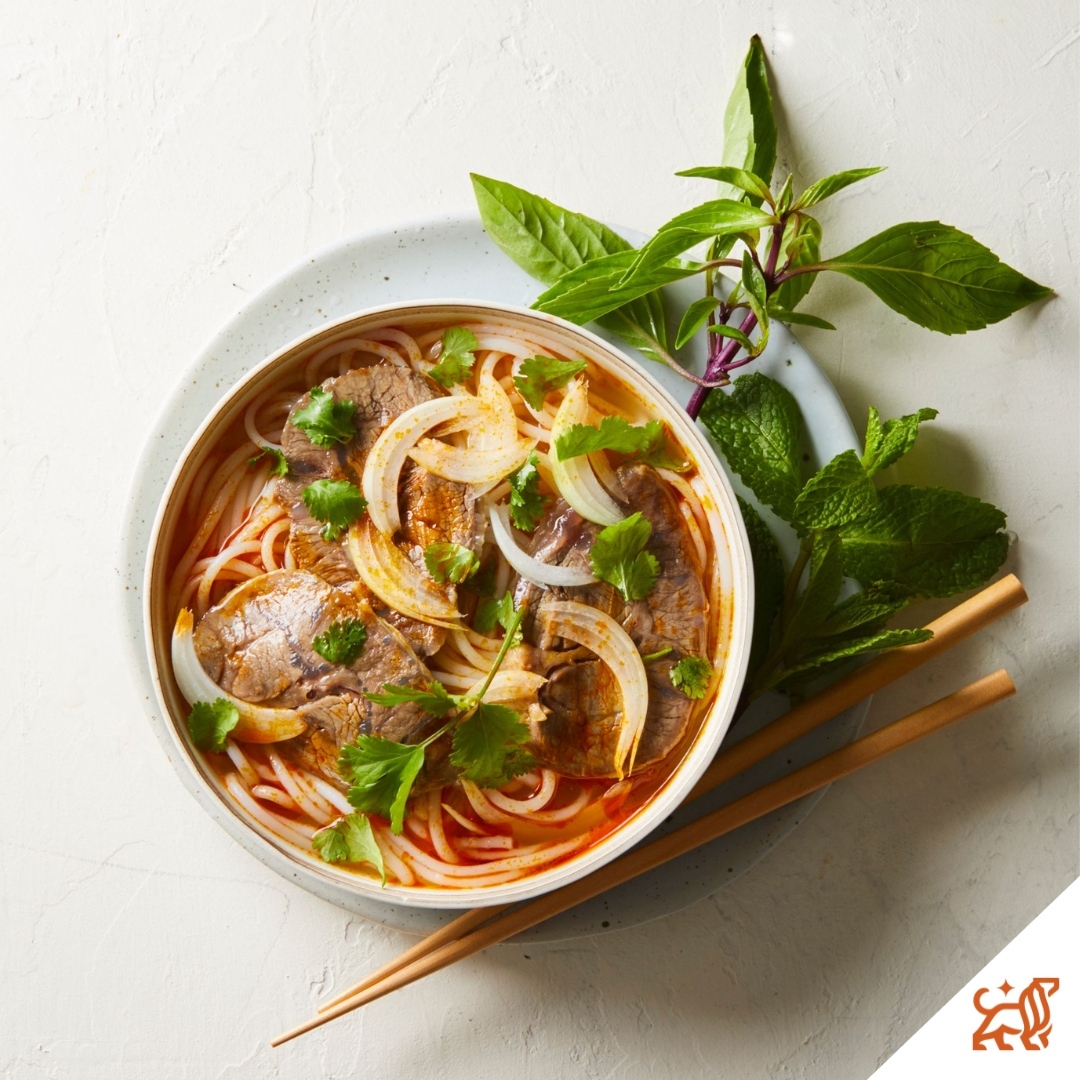 Overhead shot of steaming Vietnamese pho with beef, rice noodles, onions, and herbs, served in a white bowl with chopsticks and basil.