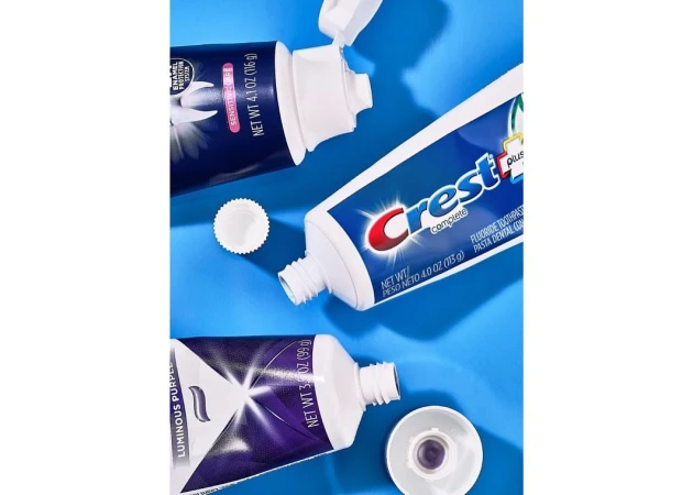 Three tubes of toothpaste, including Crest Complete and Luminous Purple varieties, arranged on a light blue background with product information.