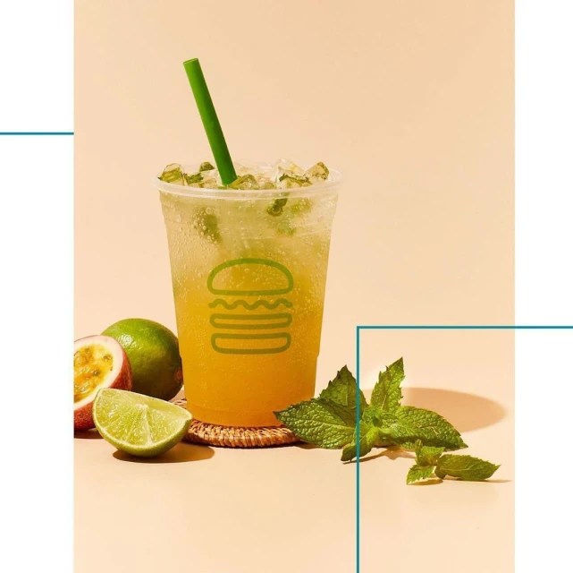 Refreshing beverage in plastic cup with straw, garnished with fresh mint and citrus fruits on a peach background.