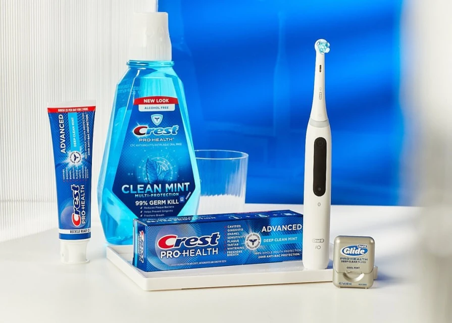 Still life shot of Crest oral hygiene products: toothpaste, mouthwash, toothbrush, and dental floss on a white surface with blue background.