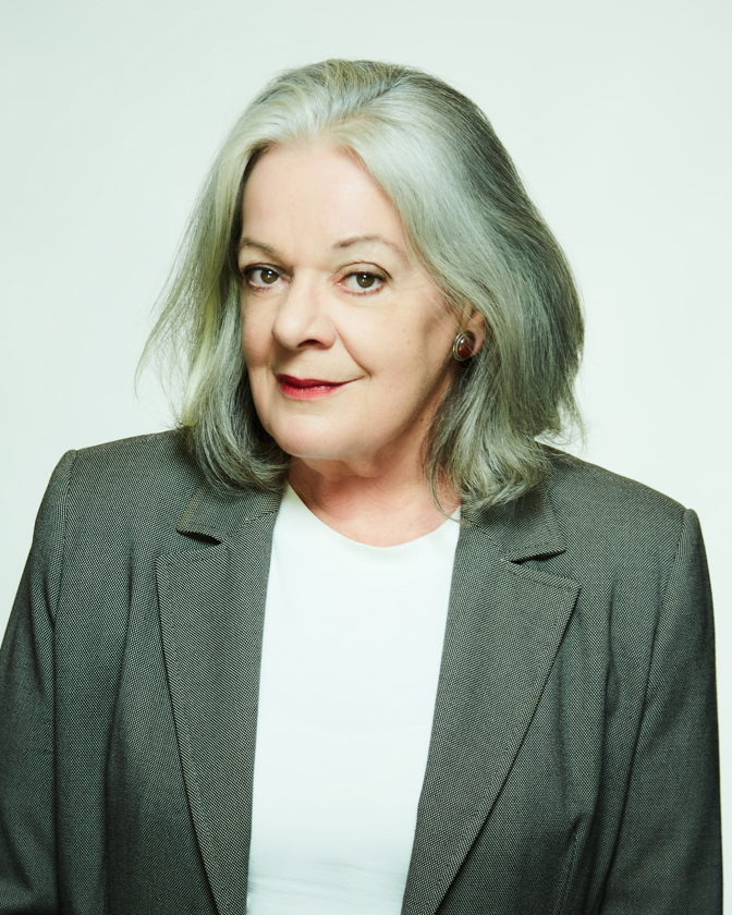 Portrait of a mature adult woman with gray hair wearing a gray blazer against a plain white background in a photo studio.