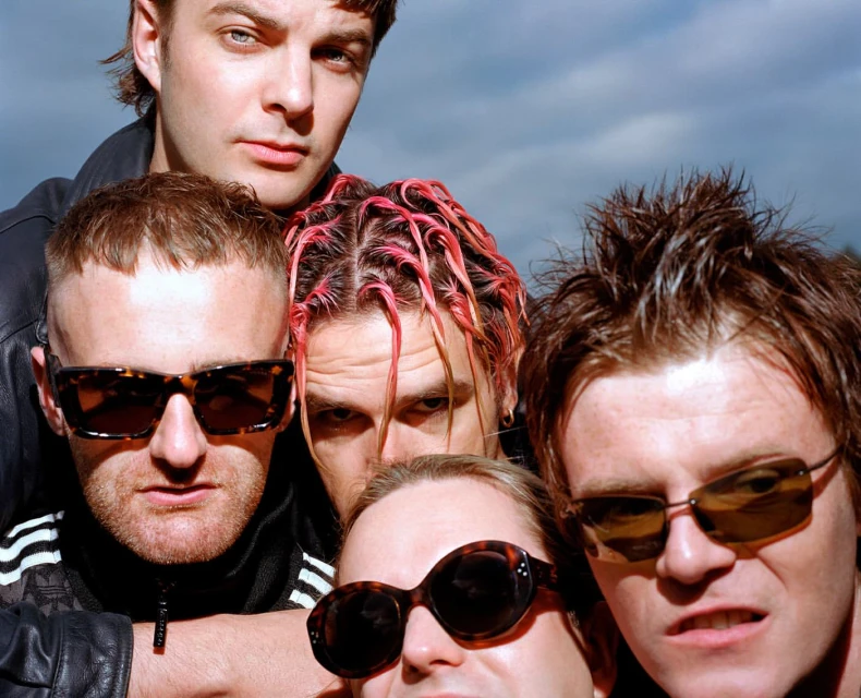 Close-up shot of five adult men wearing sunglasses outdoors, with some individuals sporting unique hairstyles and confident facial expressions.