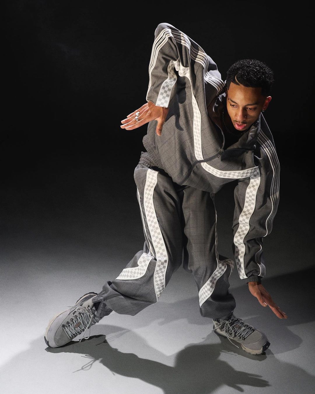 Full shot of a young man dancing in a grey and white tracksuit, striking a dynamic pose against a dark background, showcasing movement and style.