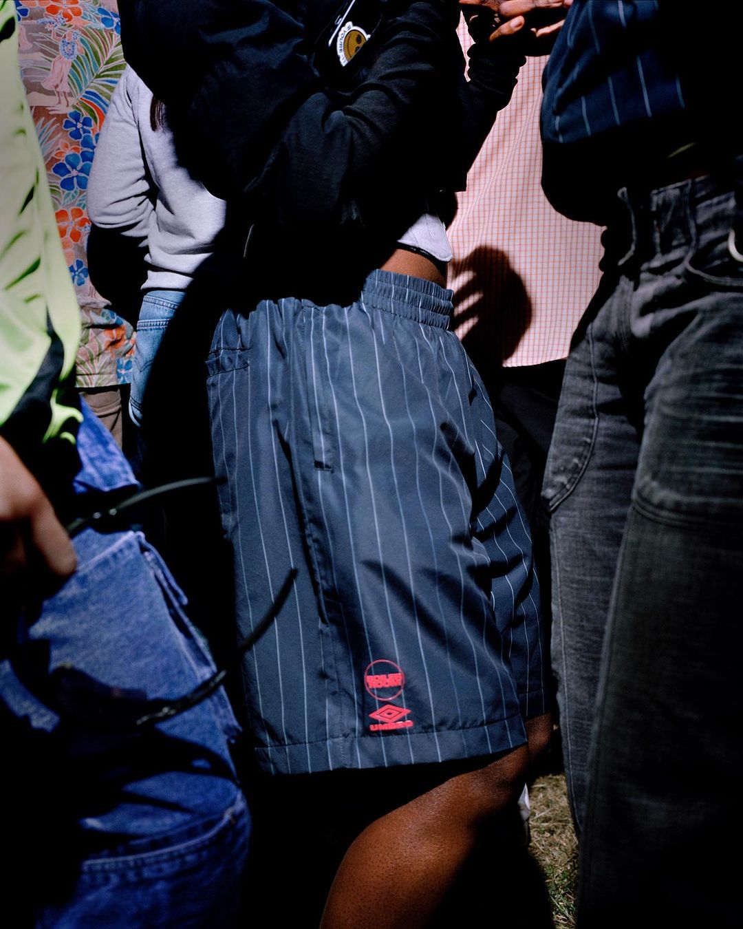 Casual street style shot with focus on navy pinstripe shorts, complemented by jeans, floral shirt, and muted tones.