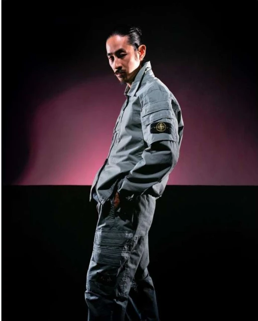 Portrait of an adult male in a grey two-piece workwear outfit posing in front of a gradient background with black and purple.