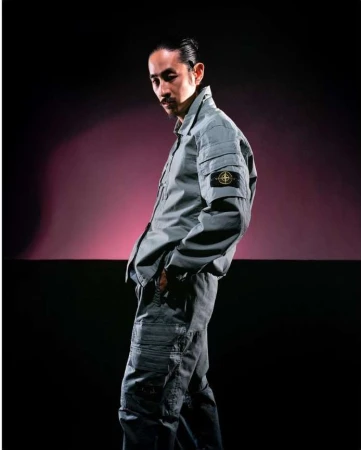 Portrait of an adult male in a grey two-piece workwear outfit posing in front of a gradient background with black and purple.