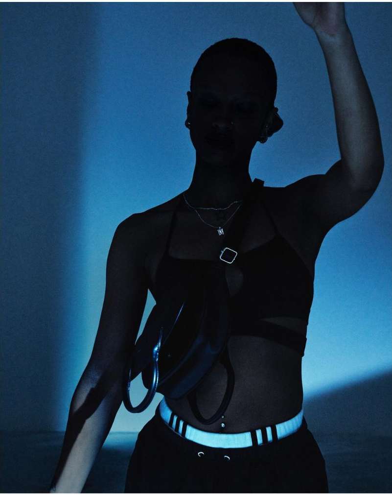 A silhouette of an adult female stands indoors against a teal background wearing athletic clothing, a reflective belt, and a chest bag.