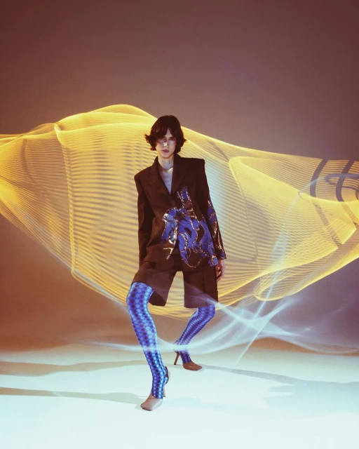 A person wearing a jacket and patterned leggings poses in front of a light painting effect backdrop with warm and cool color scheme.