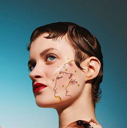 Portrait of a woman with short brown hair and red lipstick against a turquoise background, featuring artistic face drawings.