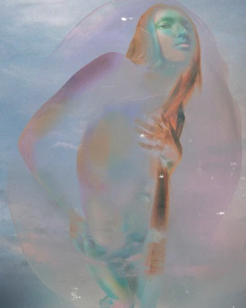 Portrait of a woman viewed through a large soap bubble with iridescent light refraction under a blue sky