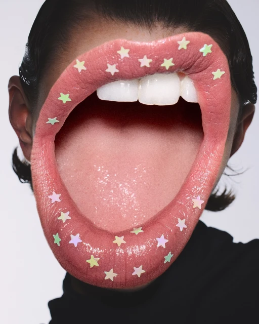 Close-up of a woman's face with an open mouth and teeth visible, decorated with star-shaped confetti on her lips and around her mouth.