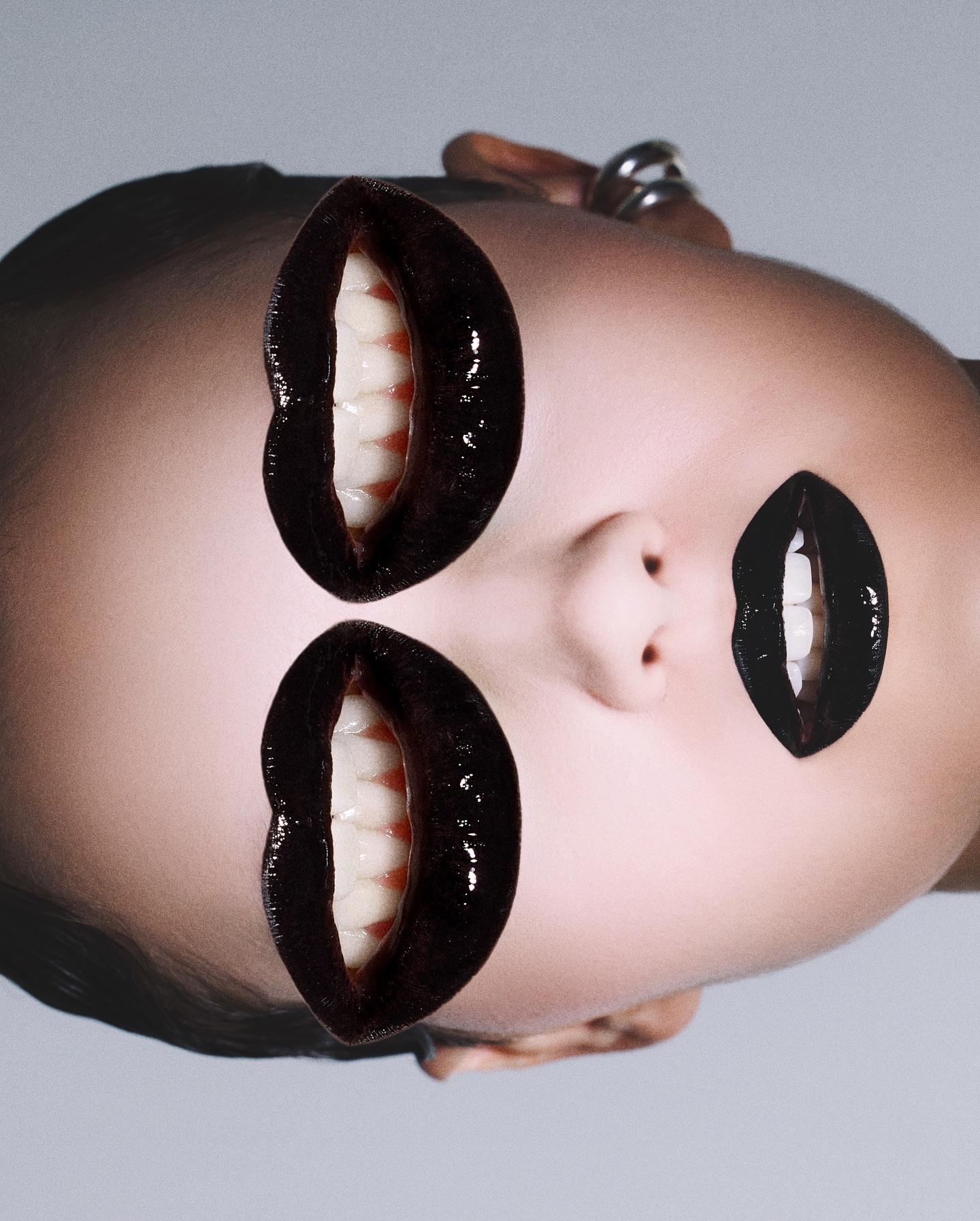 Surreal beauty portrait with an adult female face and digitally added black glossy lips with teeth, creating a multi-mouth effect.
