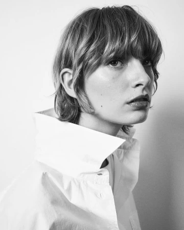 Monochrome portrait of a woman with bangs wearing a white collared shirt against a plain background
