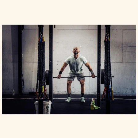 Athletic, muscular man lifts a barbell in a gym, dressed in sportswear with a determined expression. Strength and fitness training.
