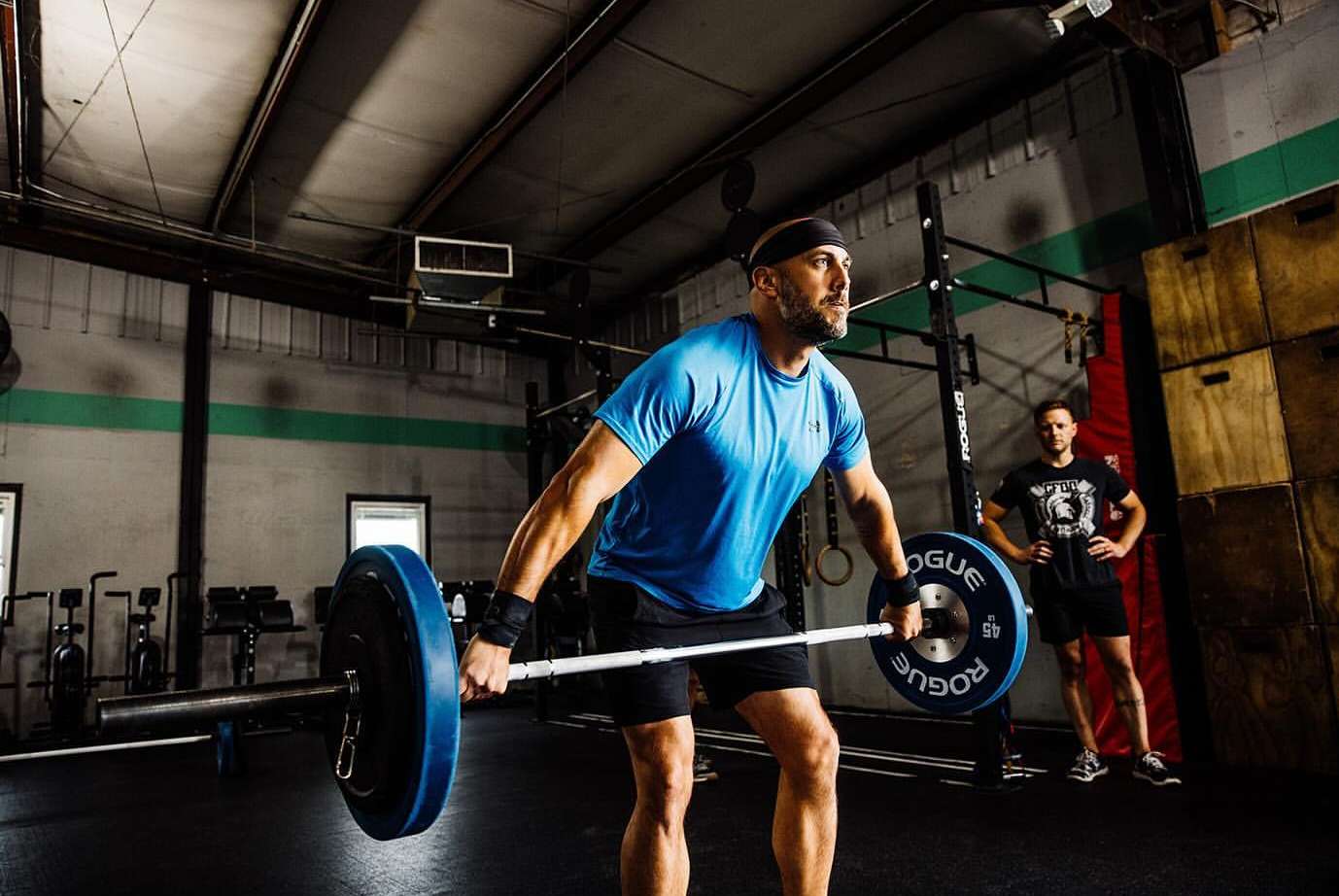 Man weightlifting a barbell with weight plates in a fitness gym. He is wearing a headband and wrist wraps and is focused on the lift.