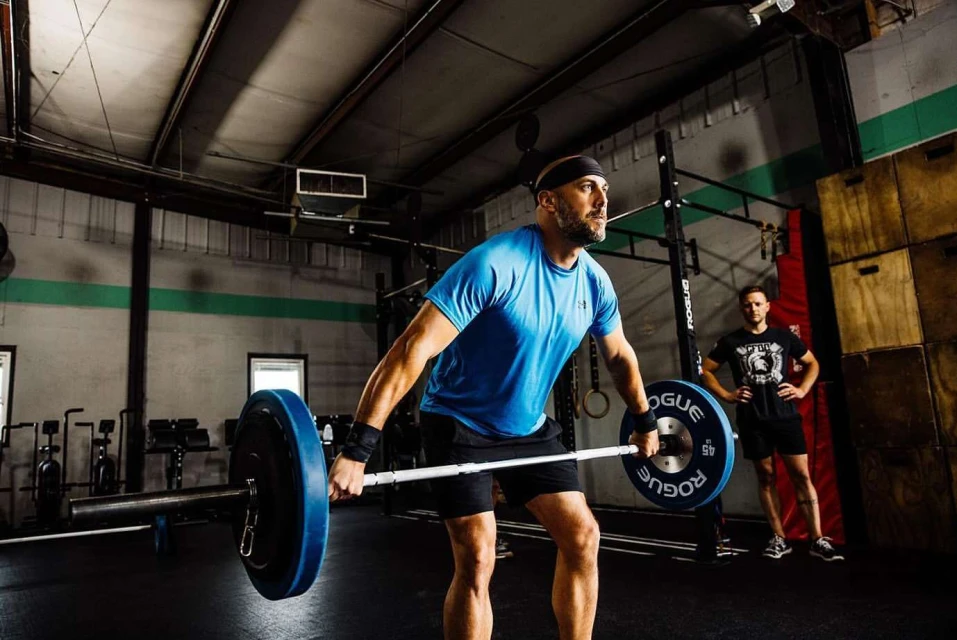 Man weightlifting a barbell with weight plates in a fitness gym. He is wearing a headband and wrist wraps and is focused on the lift.