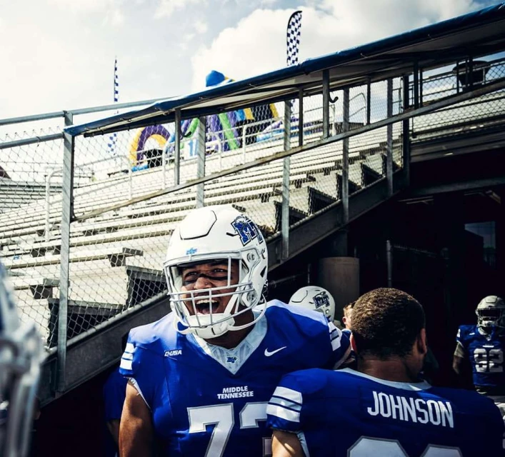 American football players in blue and white uniforms exiting the stadium. One player in the foreground is shouting with excitement.