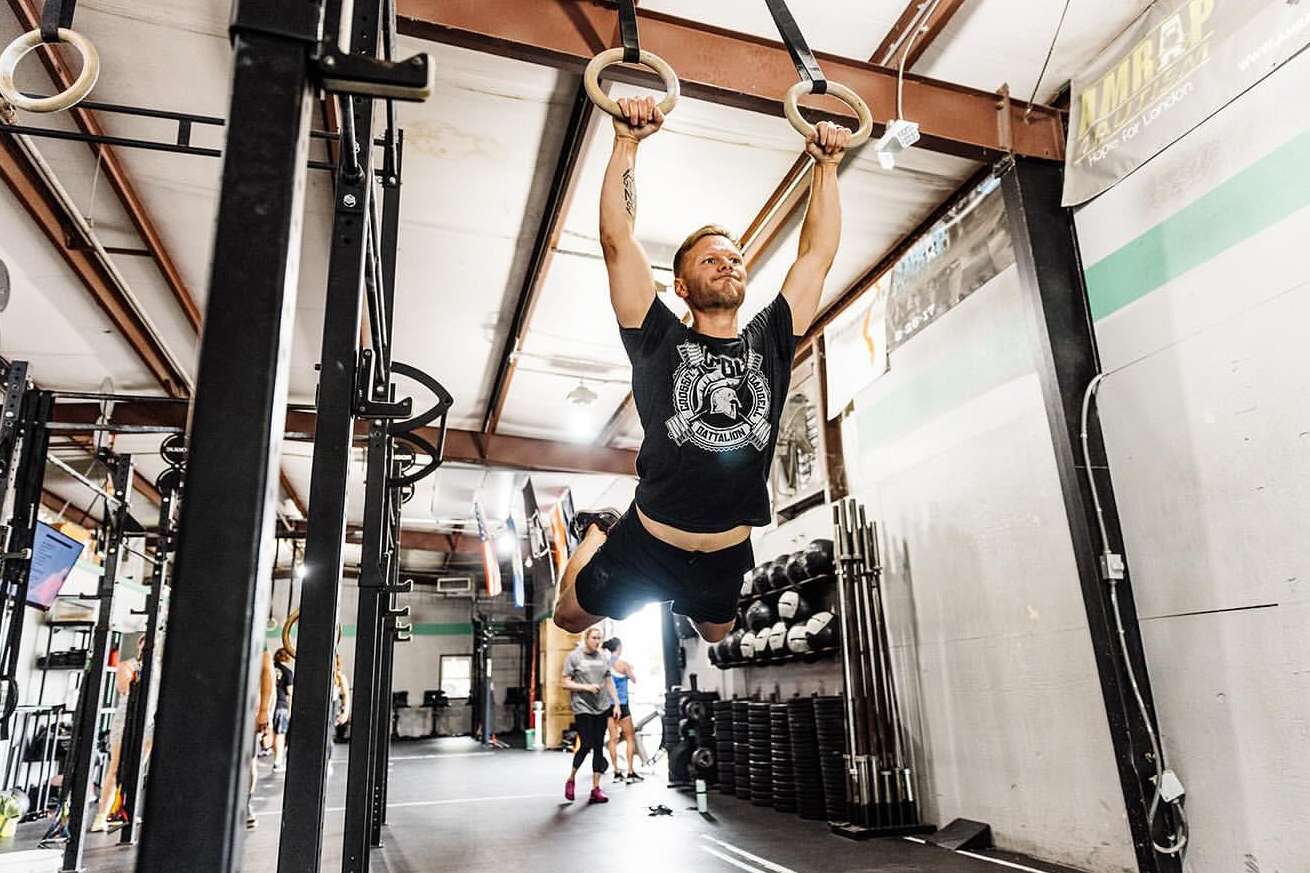 Adult male performing a gymnastic ring exercise at an indoor gymnasium, showcasing strength, fitness, and determination in a workout setting.