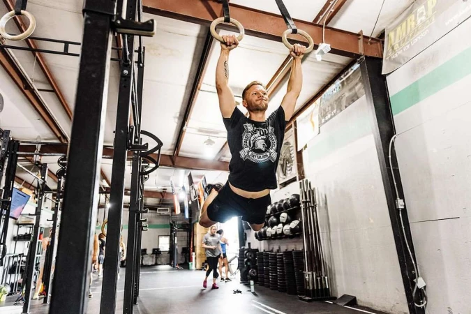 Adult male performing a gymnastic ring exercise at an indoor gymnasium, showcasing strength, fitness, and determination in a workout setting.
