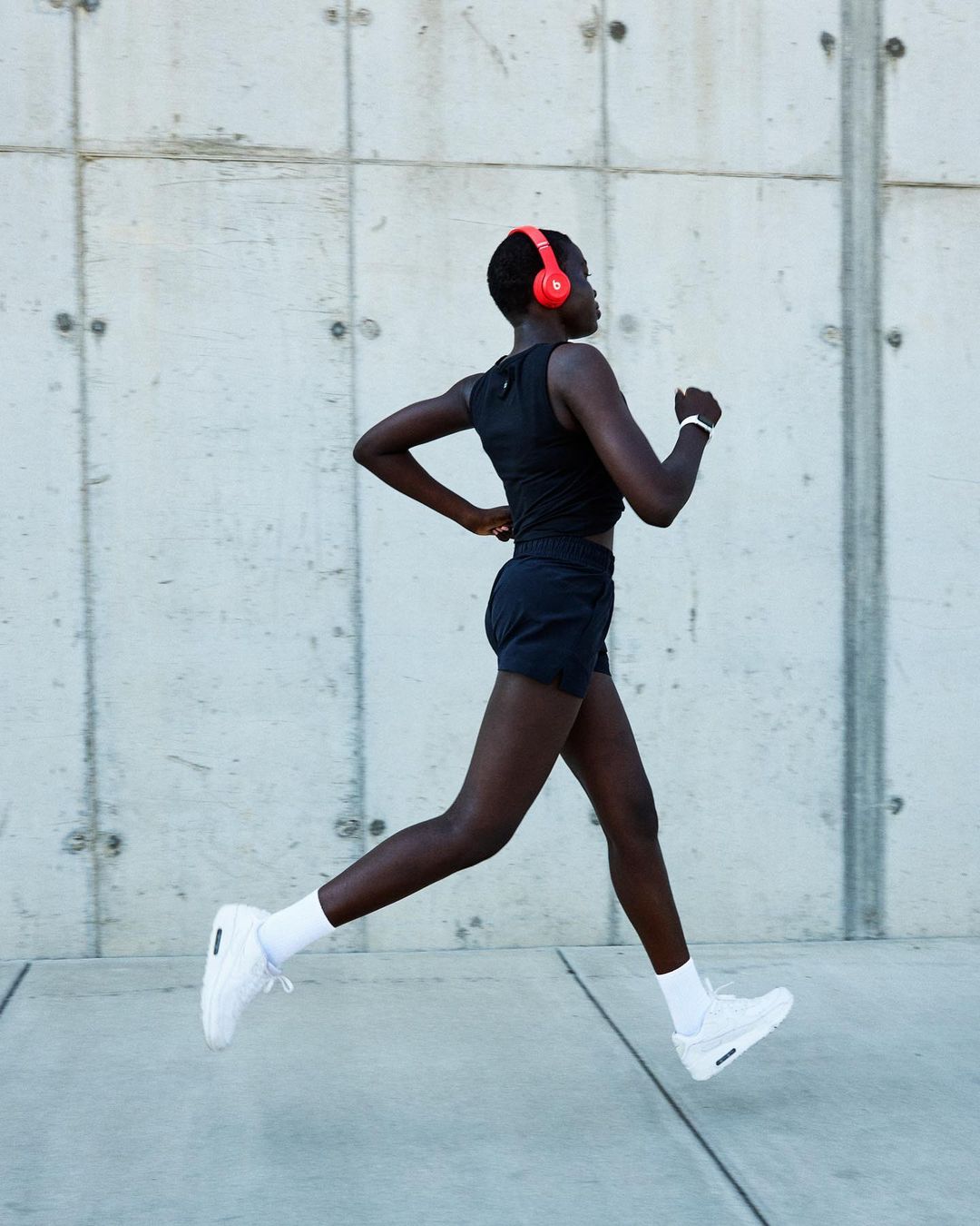 Black woman running outdoors wearing black athletic wear, white sneakers, and vibrant red headphones