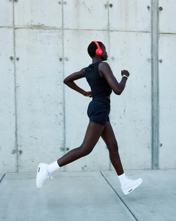 Black woman running outdoors wearing black athletic wear, white sneakers, and vibrant red headphones