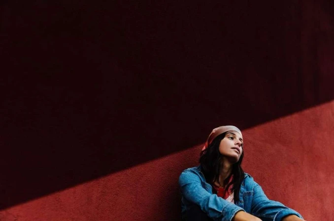 Woman wearing denim shirt and headscarf seated against a dark red textured wall