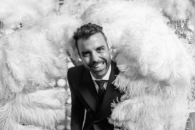 Smiling man in dark suit and tie framed by large white feathery wings, photographed by Fab Fernandez.