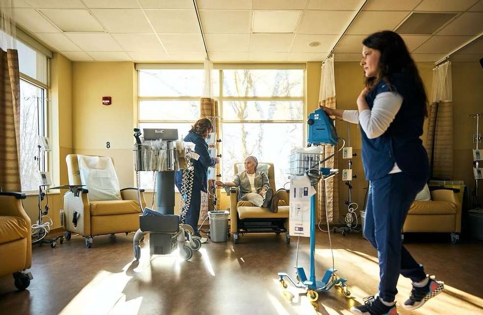 Medical professionals attending to a patient in a bright clinic room filled with medical equipment and several yellow chairs by the window.