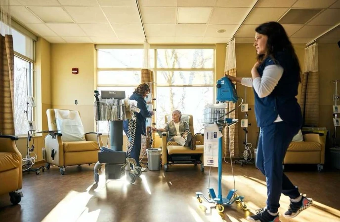 Medical professionals attending to a patient in a bright clinic room filled with medical equipment and several yellow chairs by the window.