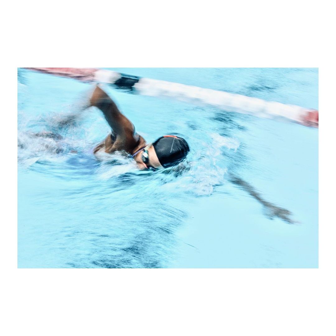 Action shot of a swimmer in a pool wearing a swim cap and goggles, capturing a dynamic moment of the sport with water splashes.